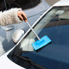 A hand is using a telescopic windshield cleaning brush to wipe the glass of a car.