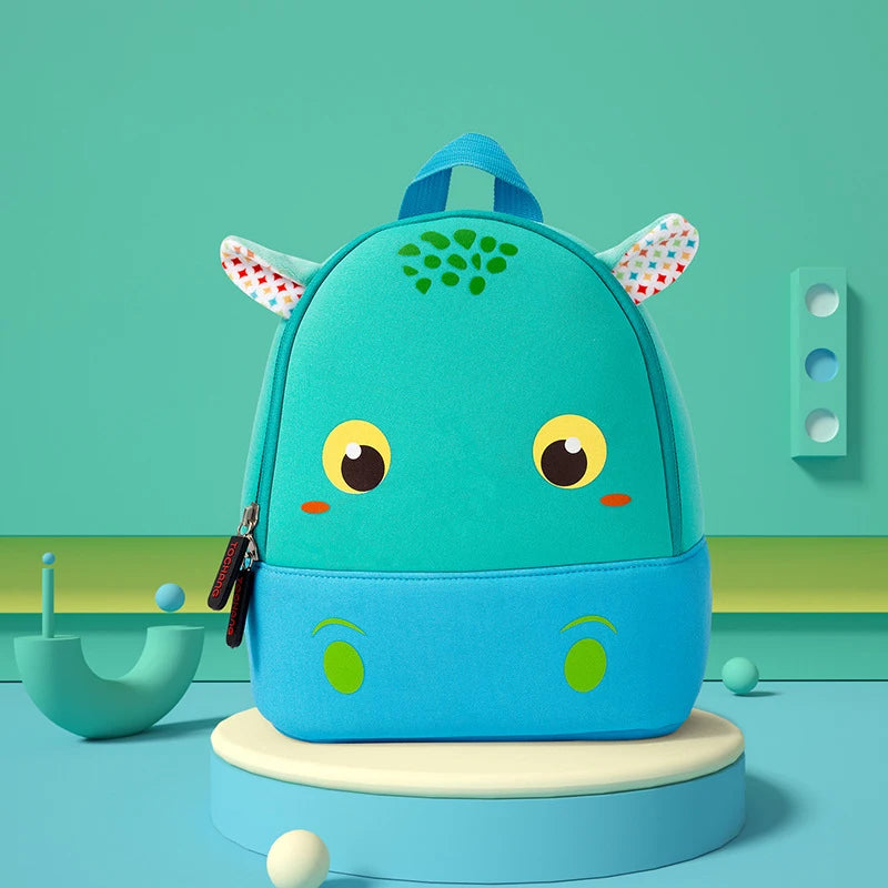A teal elephant-themed backpack for toddlers with large eyes and pink accents sitting on a light blue surface.