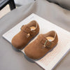 A pair of tan retro non-slip kids' moccasin shoes with a hook-and-loop closure resting on a white box.