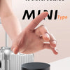 A hand is holding a compact, black magnetic suction cup phone holder with a foldable design on a white surface.