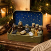 A miniature nativity scene featuring figures and animals displayed inside a gold-colored metal box with a blue starry lid.