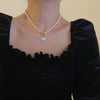A close-up of an elegant necklace featuring a pearl chain and a heart-shaped pendant worn against a black top.
