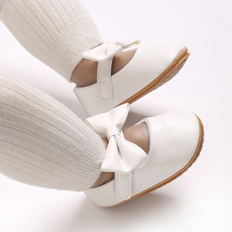 A pair of white soft non-slip baby first walker shoes worn on a person's foot.