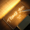 A close-up of a wooden acrylic message board illuminated by a desk lamp, with the words Thank you handwritten on it.