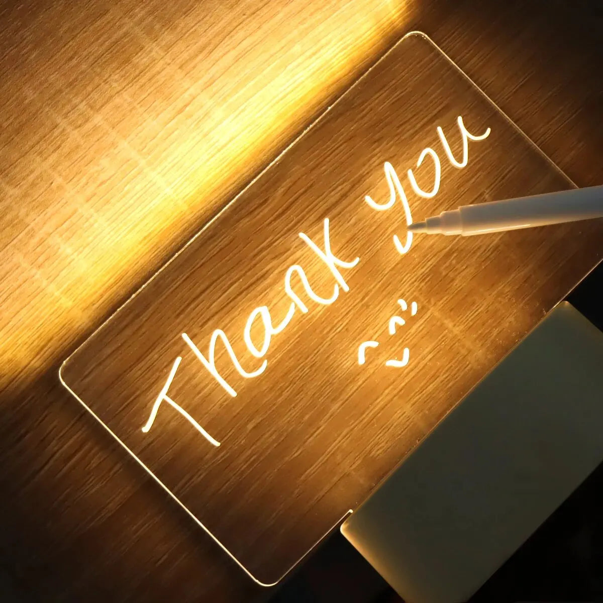 A close-up of a wooden acrylic message board illuminated by a desk lamp, with the words Thank you handwritten on it.