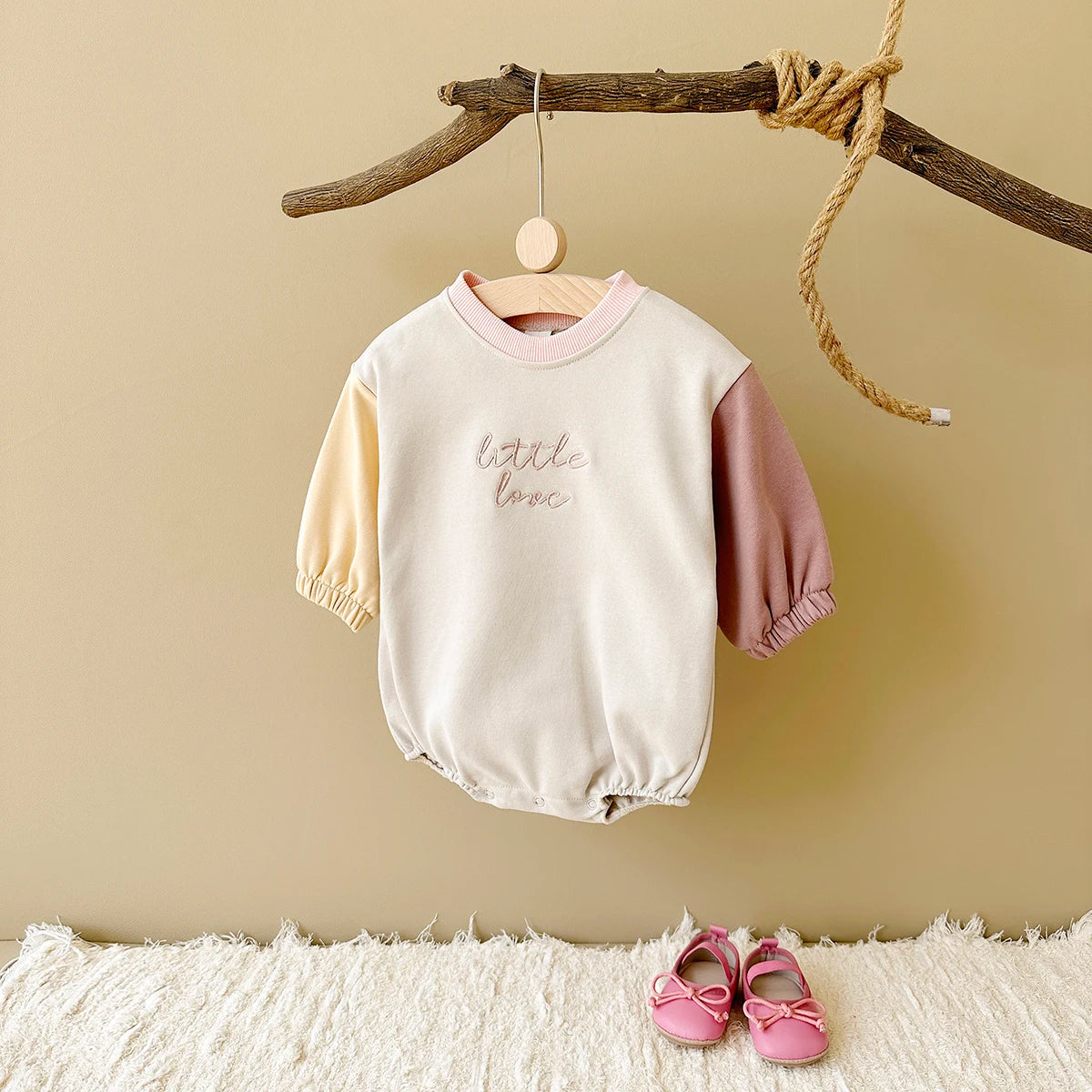 A cream and pink color block baby cotton romper hanging on a wooden rack.