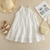 A white cotton dress with eyelet details and smocked bodice, laid out next to a straw hat and sandals.