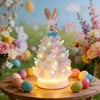Lapin de Pâques en céramique lumineux sur table en bois avec œufs colorés et fleurs.