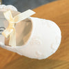A close-up of soft white baby first walker shoes with light beige ribbon and floral embroidery.