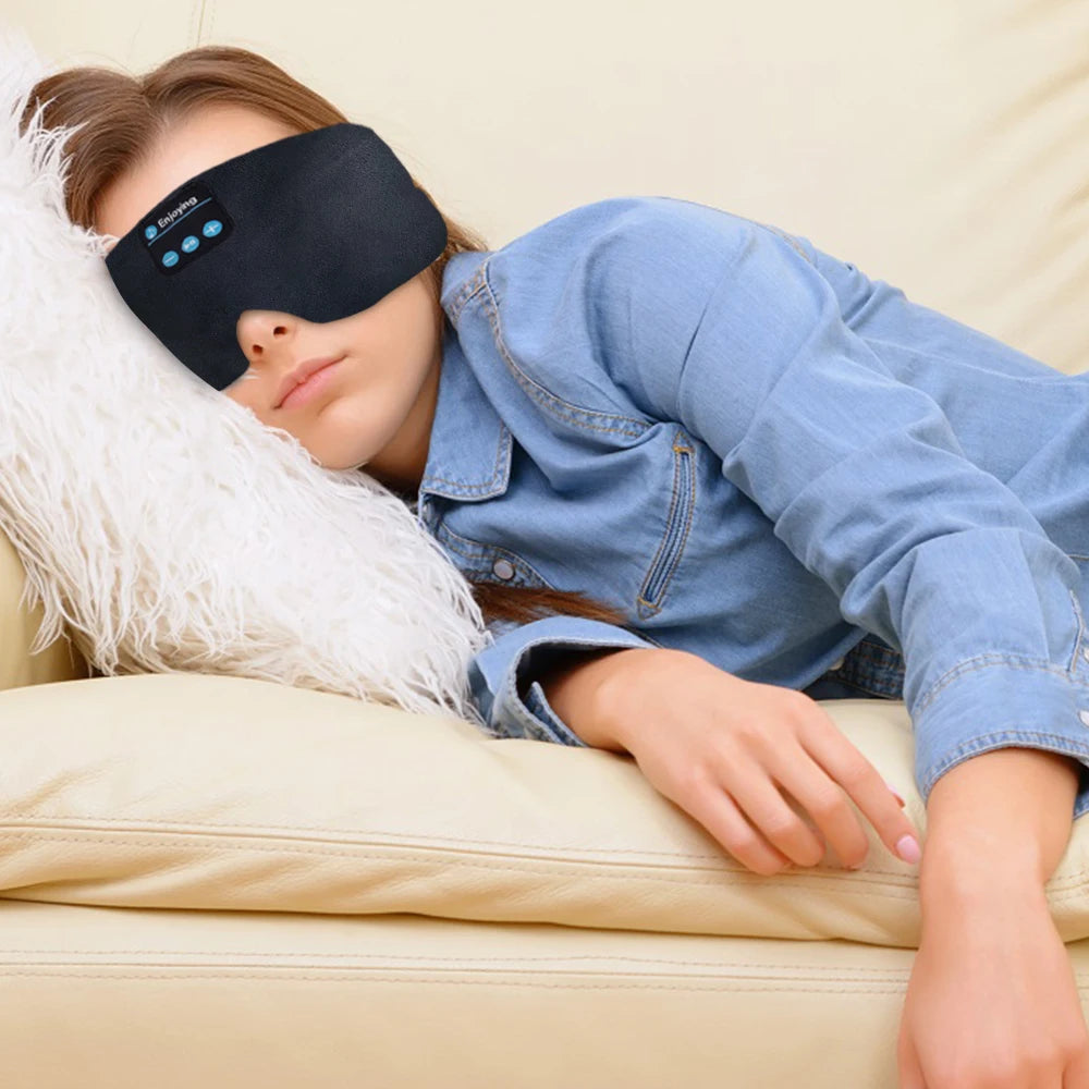 En kvinne som bruker en svart Bluetooth-søvnheadset-øyemaske mens hun slapper av i en sofa.