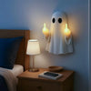 A white ghost lamp with glowing yellow hands is mounted on a wall above a wooden nightstand.