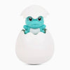 A cute, light blue frog-like toy with large eyes is emerging from a white egg-shaped container.