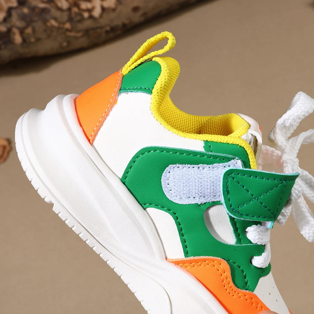 A close-up of a white sneaker with green, orange, and yellow accents and hook-and-loop closure.