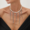 A close-up of a pearl necklace with silver tassels and small star pendants worn against a dark top.