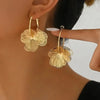 Golden double-layer hollow flower hoop earrings worn by a woman's ear.