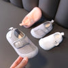 A hand holds a pair of breathable baby first walker shoes for toddlers in light gray and pink colors.