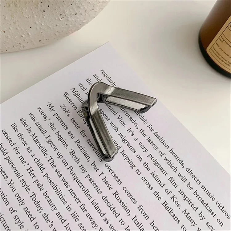 A close-up of an elegant gold V-shaped hair clip resting on a piece of paper.