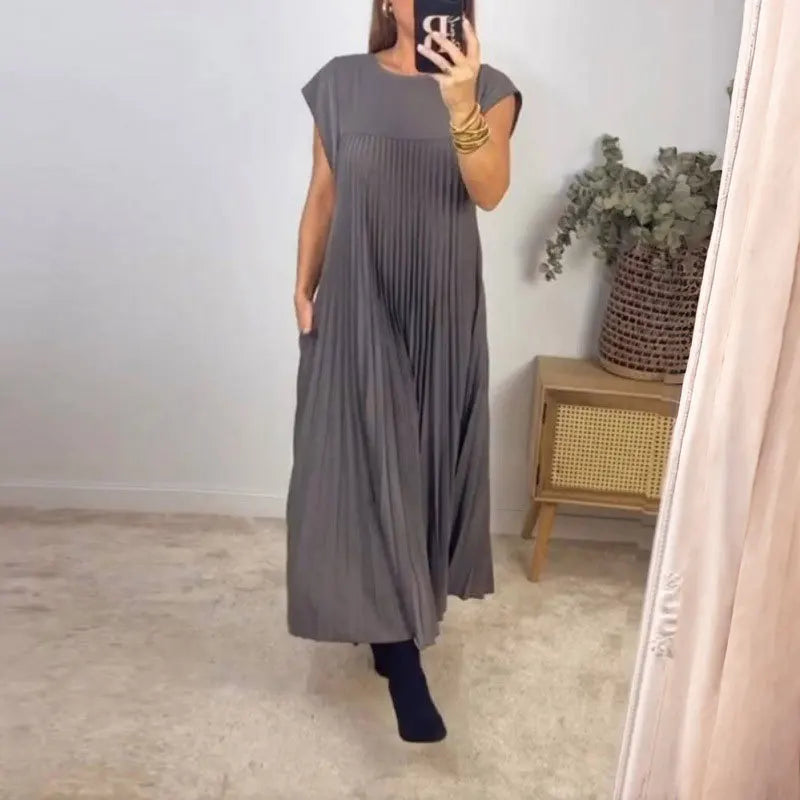 A woman wearing a sleeveless pleated midi dress in gray standing indoors.