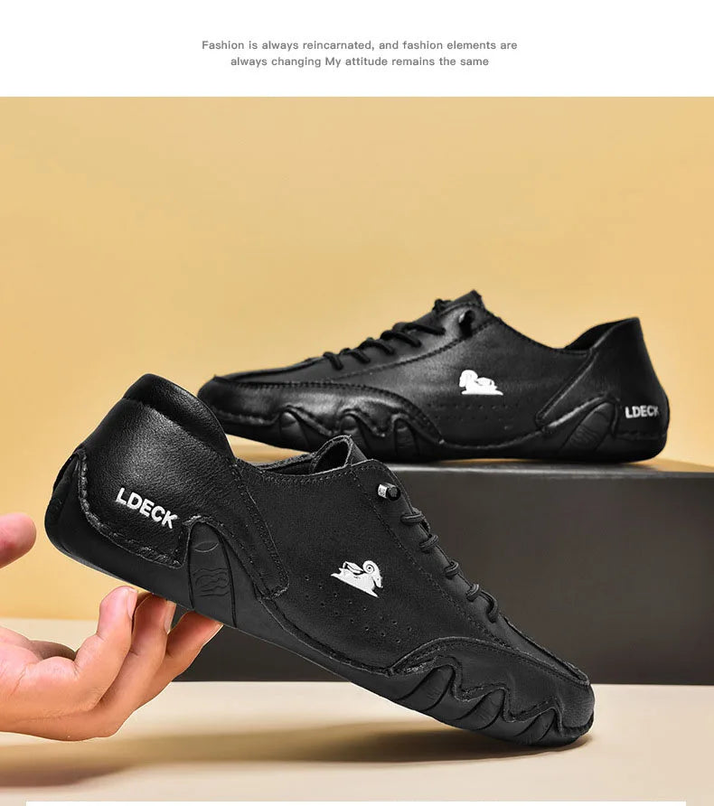 A black men's leather slip-on loafer with a white silhouette emblem is being held in a hand.