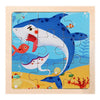 A wooden jigsaw puzzle featuring a blue and white whale swimming in blue water with small fish and yellow sand.