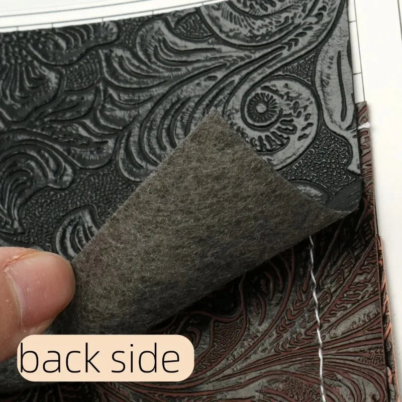 A close-up view of a dark gray textured faux leather fabric with an intricate floral pattern, being held by a finger.