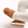 A close-up of a pair of tan suede baby winter snow boots with white knit socks and a light beige sole.