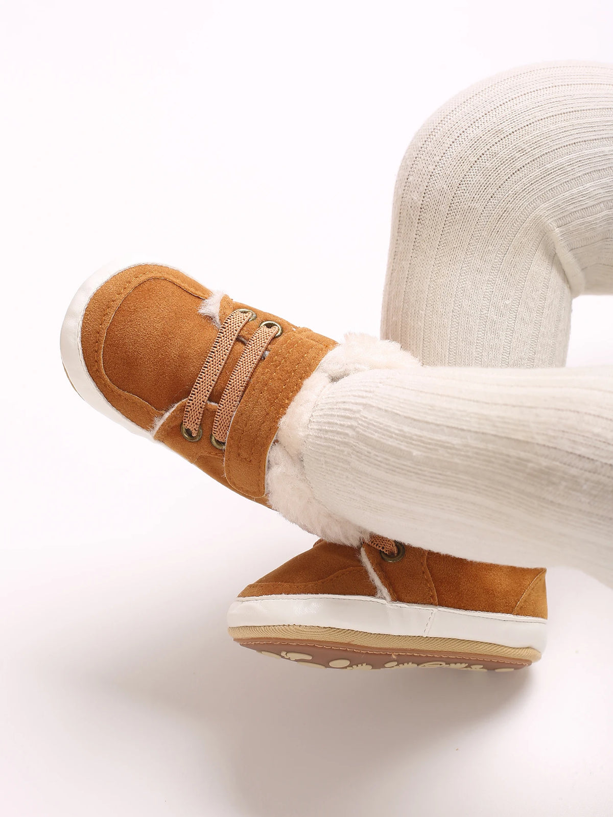A close-up of a pair of tan suede baby winter snow boots with white knit socks and a light beige sole.