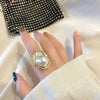 A hand wearing a gold starfish pearl ring, with a black studded clutch in the background.