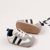 A pair of grey and white baby first walker shoes with blue stripes and a brown anti-slip sole.