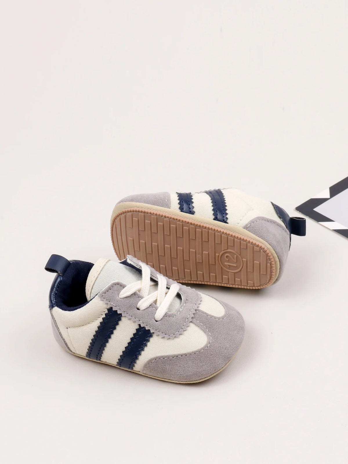 A pair of grey and white baby first walker shoes with blue stripes and a brown anti-slip sole.