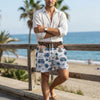 A man wearing patriotic American flag print quick-dry swim trunks standing by the ocean.