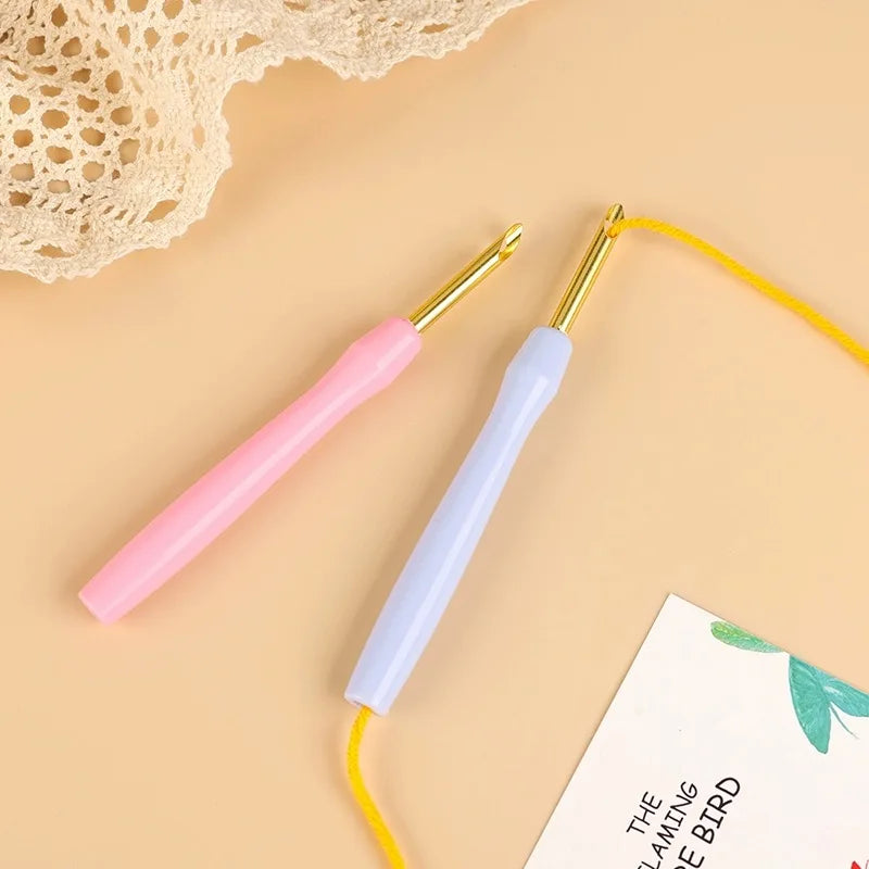 Un juego de agujas de bordado punch needle de colores arcoíris con puntas doradas y cuerdas amarillas sobre un fondo beige.