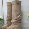 A pair of beige knee-high chunky heel boots with a metal buckle standing upright.