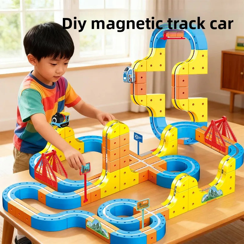 A boy is building a colorful magnetic track car maze using yellow, blue, and orange blocks on a wooden table.