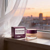 A dark purple jar of Calcium Dark Spot Eye Cream sits on a windowsill with soft natural light.