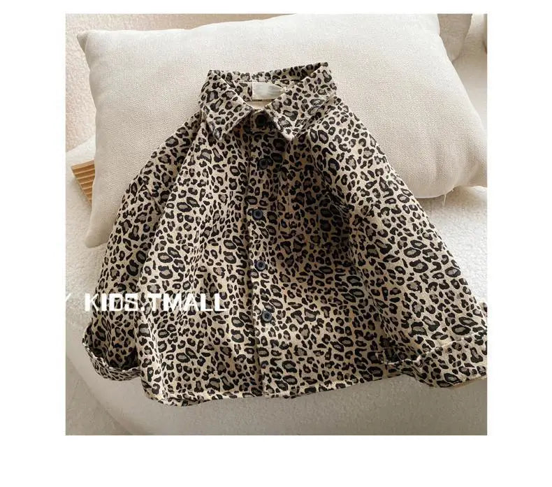 A close-up of a boy's leopard print denim shirt folded on a light-colored cushion.