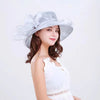 A woman models a silver wide brim organza sun hat with ruffled mesh and a white lace top.