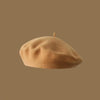 A light tan wool beret hat resting on a plain brown background.