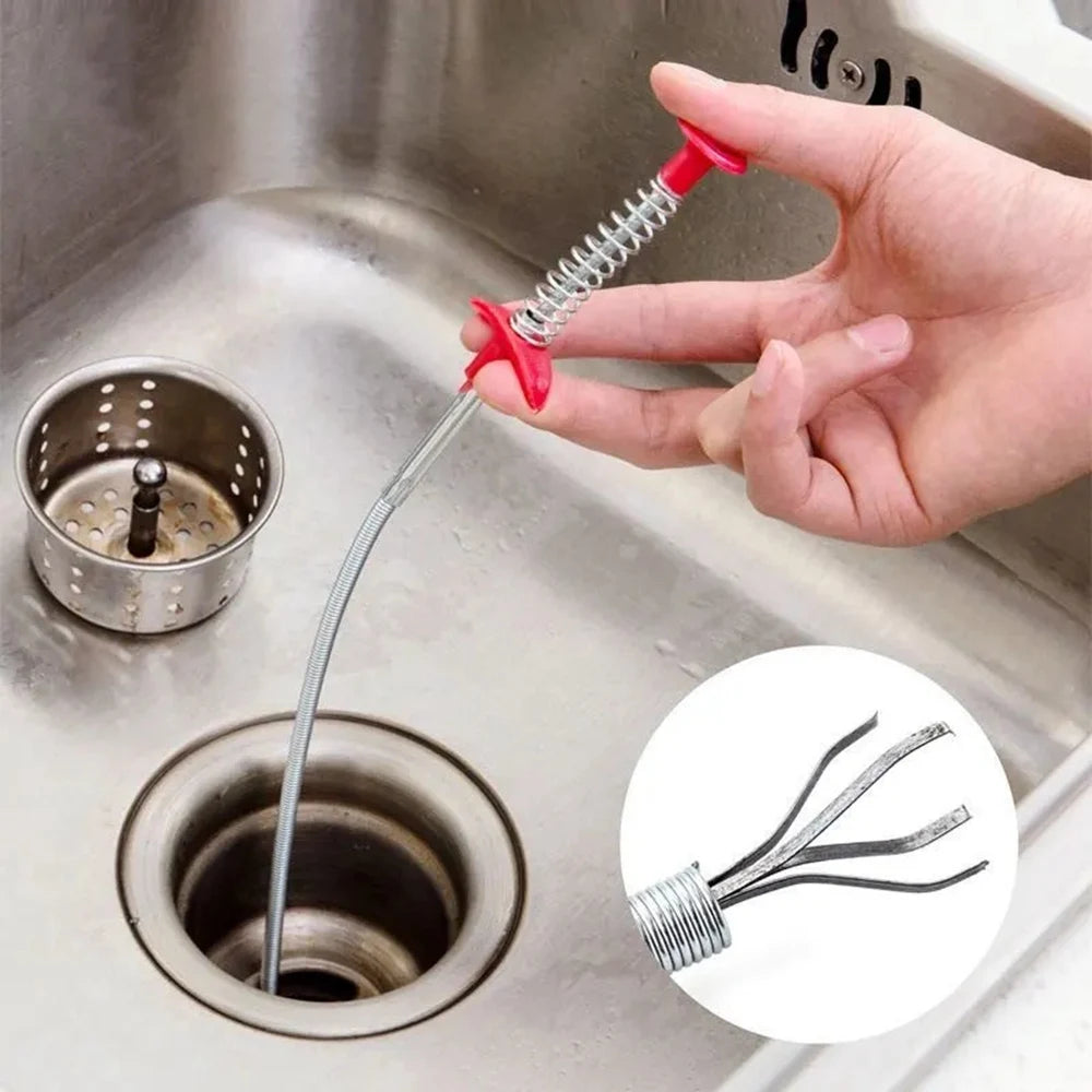 A hand is using a flexible drain snake tool to clear a clogged sink drain.