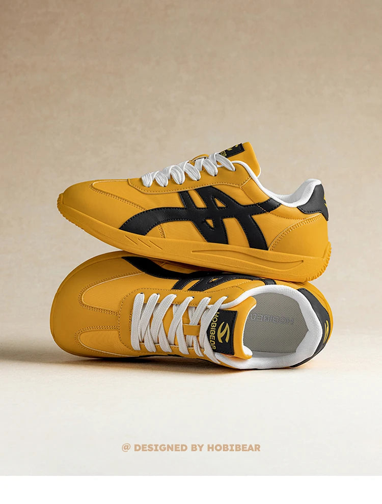 Ein Paar gelb-schwarze Adidas-Sneaker mit weißen Schnürsenkeln auf hellbeigem Untergrund.
