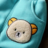 A light turquoise fleece pajama top featuring a cute yellow bear design on the chest.