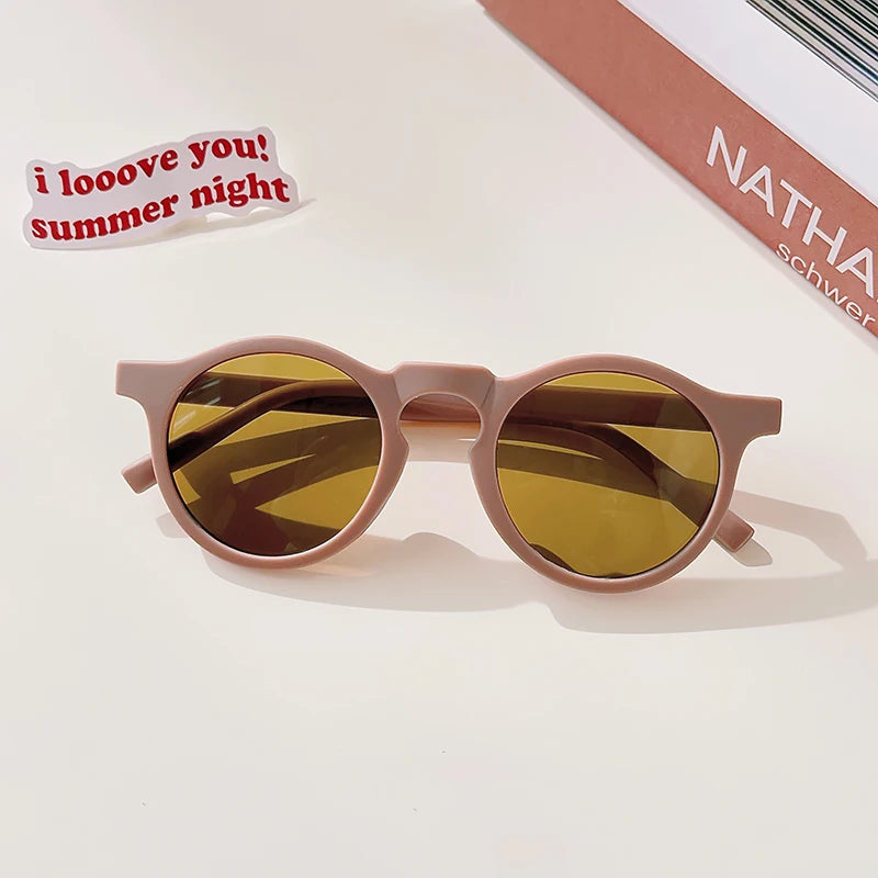 A pair of light pink sunglasses with amber lenses resting on a white surface.