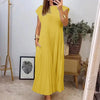 A woman wearing a bright yellow sleeveless pleated midi dress with a round neck, standing indoors.