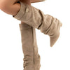 A pair of taupe knee-high chunky heel boots with a metal buckle worn on a foot.