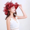 A woman wearing a white lace top and a large red ruffled organza sun hat.