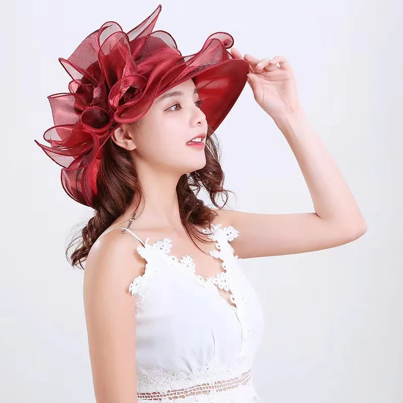 A woman wearing a white lace top and a large red ruffled organza sun hat.