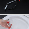 A hand is using a flexible drain snake tool with a red handle and metal tip to clear a clog in a toilet bowl.