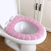 A pink soft acrylic toilet seat cover is placed on a white toilet bowl.