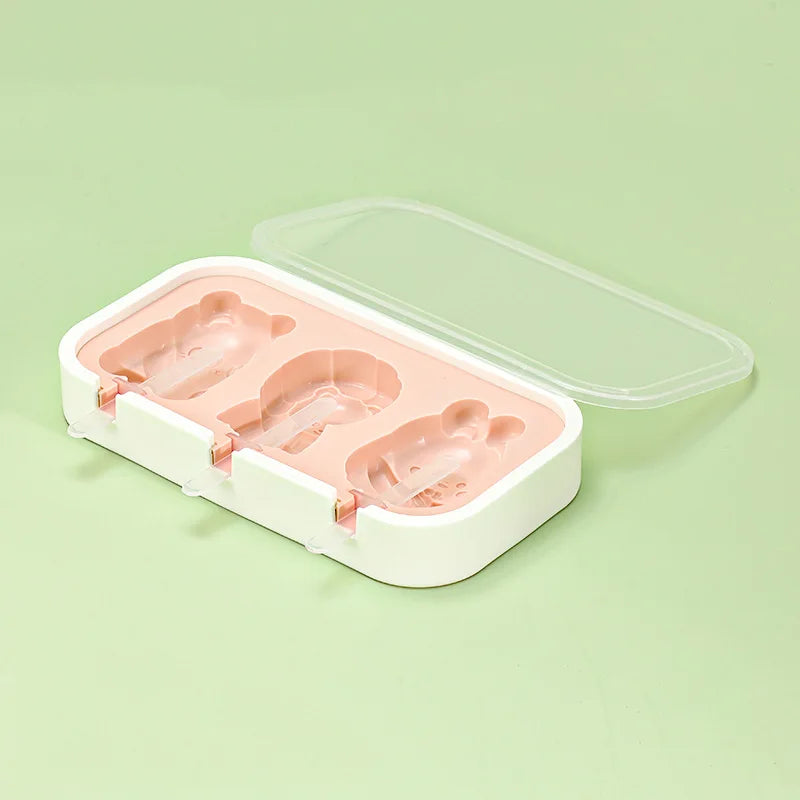 A white silicone mold tray with a clear lid containing three pink popsicle molds.