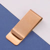 A rectangular rose gold metal tie clip lying on a blue-gray surface.